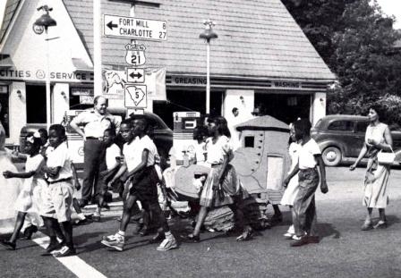 Local students attending the 1952 Rock Hill Centennial Parade walk in front of the filling station where Mrs. Roddey’s flower garden had once been found.