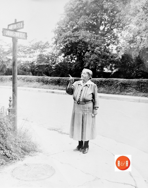 Mrs. Kate Hutchison (the widow of David Hutchison), points to the road sign at the corner of Hampton and Johnston Street.